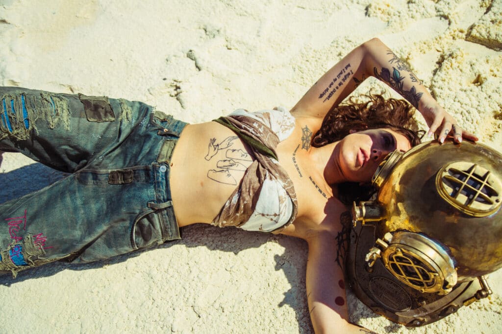 model lying on beach with brass diver’s helmet